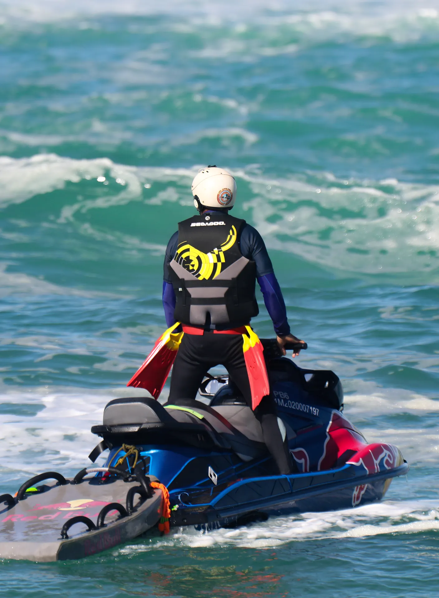 Resgatista em pé no jet ski, de frente para as ondas, com as nadadeiras na cintura